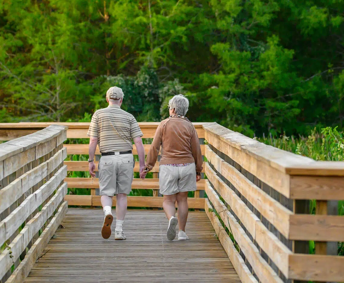 Couple walking together on scenic wooden path surrounded by greenery.