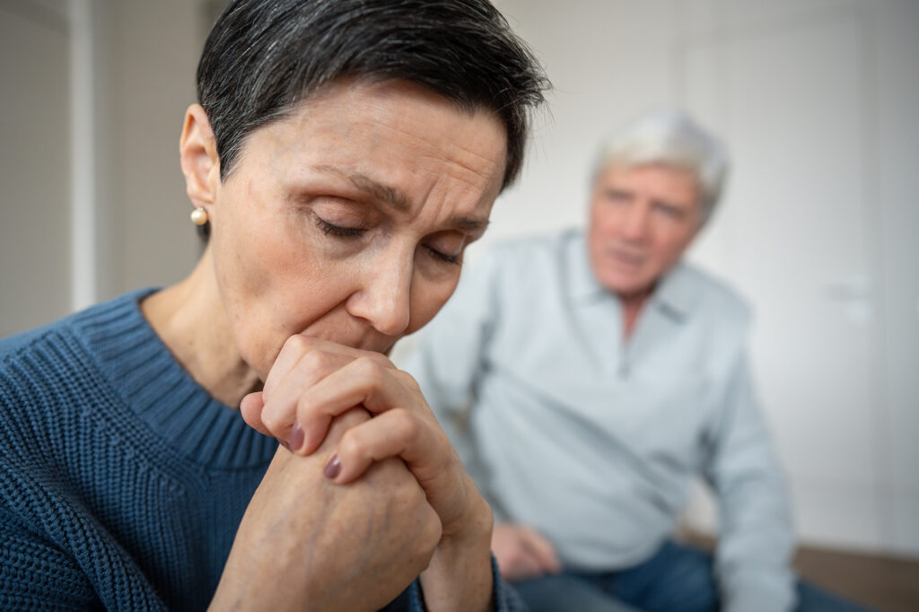 A tired and sad caregiver sits near her senior dad