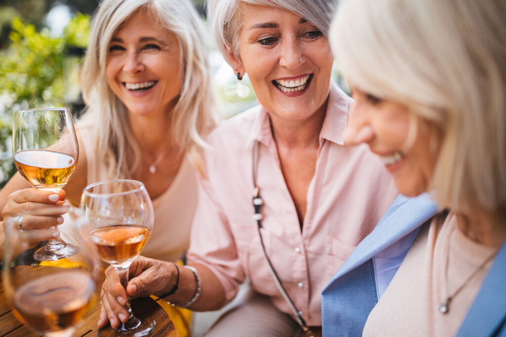 Smiling senior female friends enjoying a glass of wine together outside